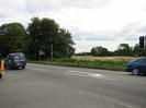 Road with trees and field beyond.
Traffic lights on right.