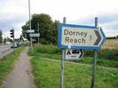 A4 Bath Road on left with traffic lights and queue of vehicles.
Signs on street-light pole for Taplow and Taplow Station.
Grass verge with footpath.
Sign in foreground for Dorney Reach.
Small sign for caravan and campsite.