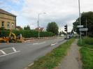 Looking east on the A4 Bath Road.
Three-storey building on left with police badge in bas-relief on top floor.
High hedge along road.
Roadworks with yellow dump-truck and digger.
Red and white safety barriers.
Queue of cars at traffic lights.
Road signs for Taplow Station and Taplow.
Grass verge on right with footpath and trees.