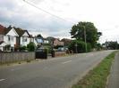 Road with grass verge and pavement on near side.
Row of houses on far side.
Roadsign warning of Z-bend.