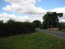 Looking north on Marsh Lane.
Large grassy area in the foreground, road and trees in the background.