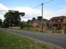 Looking north on Marsh Lane.
Road and grass verge in foreground.
Brick walls and brick-built houses in the background.