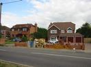 Road in the foreground. Low brick wall and builders equipment.
Houses and cars in the background.