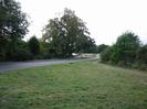 Looking south on Marsh Lane.
Grassy area and road. Trees in the background.