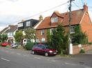 Road with row of houses.
Nearest house is of red brick with red tile roof.