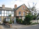 End of a row of terraced houses on the left. Three-storey brick building on the right with large tree in front.