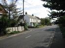 Looking south on Marsh Lane.
Entrance to Ye Meads is visible on the left, with white-painted houses beyond it.
Road with footway on each side and trees to the right.