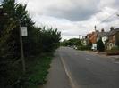 Looking north on Marsh Lane.
Hedge and footway on left with bus-stop sign.
Road with houses on the right.