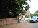 Road with footway and parked van.
Low brick wall with dark trees and house behind.
Pile of building materials.