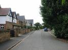 Looking west on Ye Meads.
Road with footway and houses on the left.
Dark trees on the right.