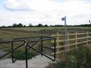 Steel kissing-gate and fence.
Cycleway sign.
Fence and scrubby grass.