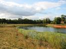 River with scrubby grass bank on left.
Orange mesh enclosures on far side of river, with house set among trees beyond.