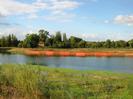 RIver with orange mesh enclosures on far side.
House set among large trees in the background.