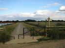 Entrance to path.
Black metal kissing-gate, wooden rail fence.
Wooden signpost on right.
Wide path straight ahead with river on left.