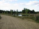 Wide gravel track with row of posts on the right and river beyond.
Trees in the distance.