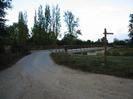 Road leading to bridge across river.
Wooden signpost on right.
Tall Poplar trees in the background.