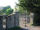 High stone wall with ornate wrought-iron gates and lamps.
Trees on the right.
