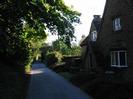 Narrow lane with stone-built house on the right and trees on the left.