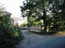 Junction of two lanes with group of houses.
Trees on the right.