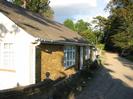 Bungalow with white-painted end wall and sandy-brick side wall.
Grey slate roof.
Gravel track to the right.
