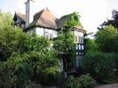 Wey Lodge: two-storey house with white walls and black timbers.
Tiled roof with ridge ornaments.
Creeper growing on house.
Bushes around.