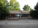 Car-park and entrance to Thames Valley Adventure Playground.
Wire fence with gates.
Long low building with grey roof surrounded by trees.