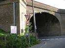 Brick arch railway bridge.
Embankment on left with telephone pole and signs:
"GIVE WAY", 40mph speed-limit, advert for the Maypole Pub.
Street-light behind telephone pole.