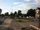 Looking west on the A4 Bath Road.
Road on the left with bus stop on near side.
Low wooden railings.
Harvester pub sign for the Dumb Bell.
Sign in grass: "2 course Sunday Spit Roasts 6.95"
Car-park with pub builidng on far right.