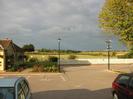 Car-park with harvester restaurant building on left.
White picket fence with playing fields beyond.
Large tree on right.
