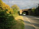 Looking east on the A4 Bath Road.
Tarmac pavement on left with grass verge and row of trees.
Large brick arch railway bridge in the background.