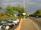 Looking east along the A4 Bath Road.
Cars on dealership forecourt on left.
Small trees, low brick wall around forecourt.
Wide tarmac pavement with street lights.
Road with railway bridge in the distance.