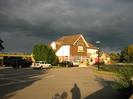 The Dumb Bell Harvester restaurant.
Car-park with cars.
Restaurant building has two stories with a tiled roof.
Fields visible behind.
Photographer's shadow on car-park.