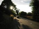 Looking west on Approach Road.
Railway embankment with trees on left.
Pavement and road.
Cars on road.
Trees on right.