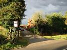 Driveway to red-brick two storey house.
Trees on both sides.
Estate agent's sign.