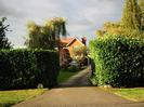 Driveway to two-storey red brick house with red tiled roof.
High hedges on both sides.
Stone on left with number 2.
