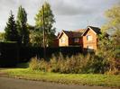 Red-brick house with red tiled roof.
Hedges and trees around house.
Telephone pole.