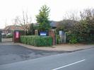 The Bishop Centre main gate.
Metal gate on left, set between high brick pillars.
Low hedge with sign above: "BISHOP CENTRE".
Electricity sub-station.
Large buildings in the background.