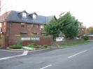 Bishop House: three storey brick office building with dark roof.
Low walls around car-park, with small trees.