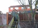 High fences and garden gate with house behind.
Trees on the right.
Steps up to gate.